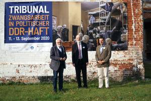Photo (from left to right): Karl Hafen, Thomas Schirrmacher and Dr. Sorin Muresan in front of the poster of the tribunal and the outside wall of the former Cottbus penitentiary Â© BQ/Martin Warnecke